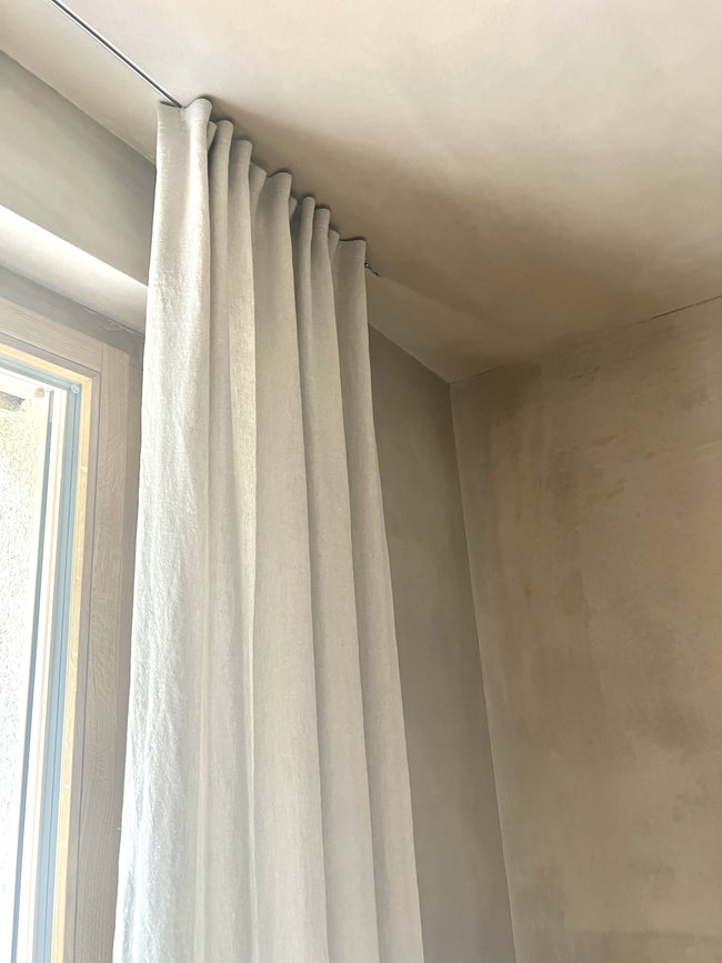 Closeup of curtain in the linen fabric scandi rice against a mineral-plastered wall – Discover the seamless blend of scandi rice linen with a matching mineral plastered background.